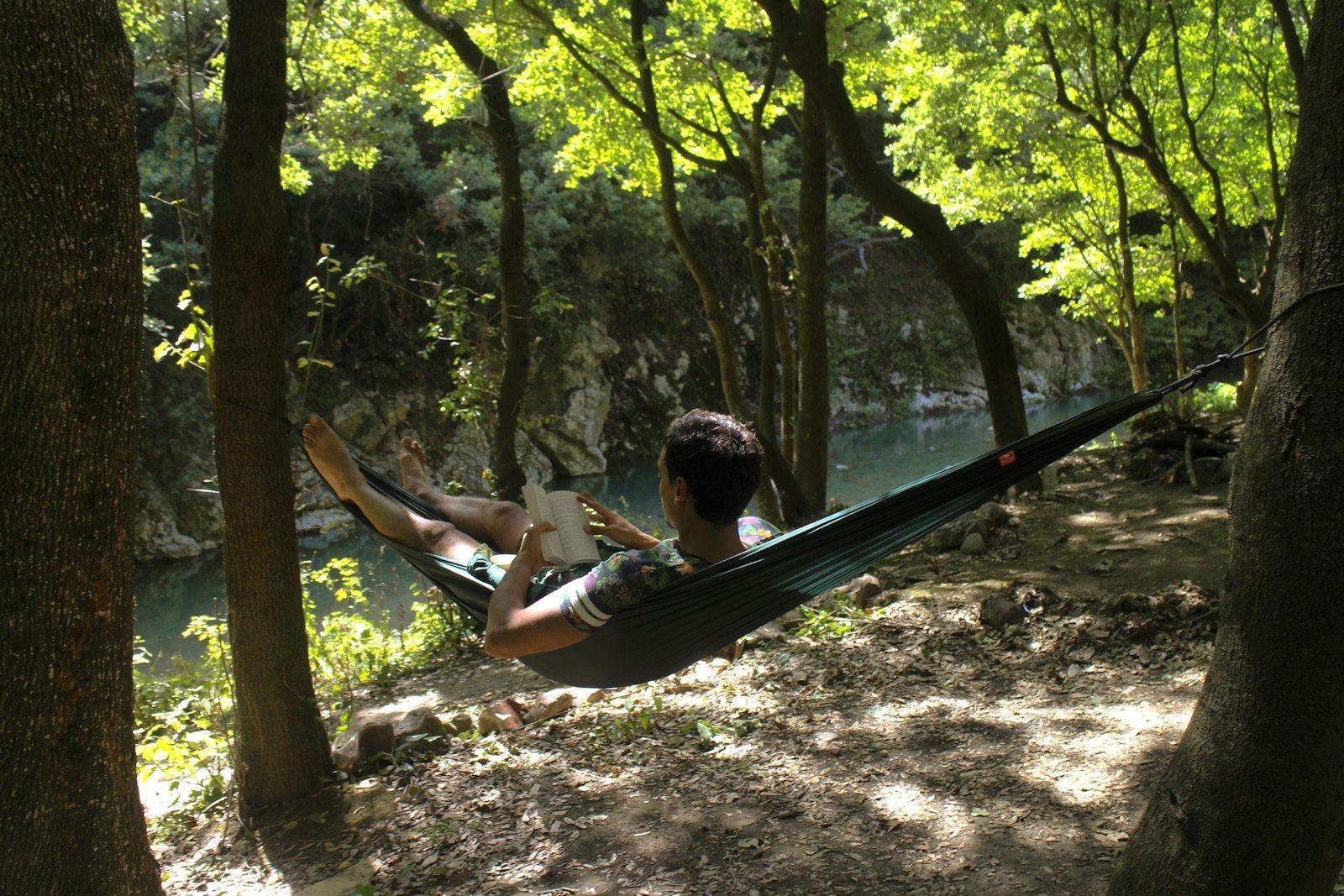 man lying down on hammock while reading book near river