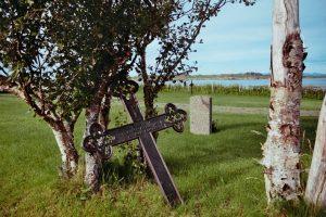 A wooden cross sitting in the grass next to a tree